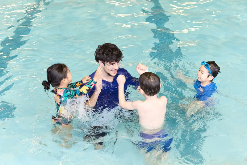 A swim teacher in the water leads a small group of children through a lesson.