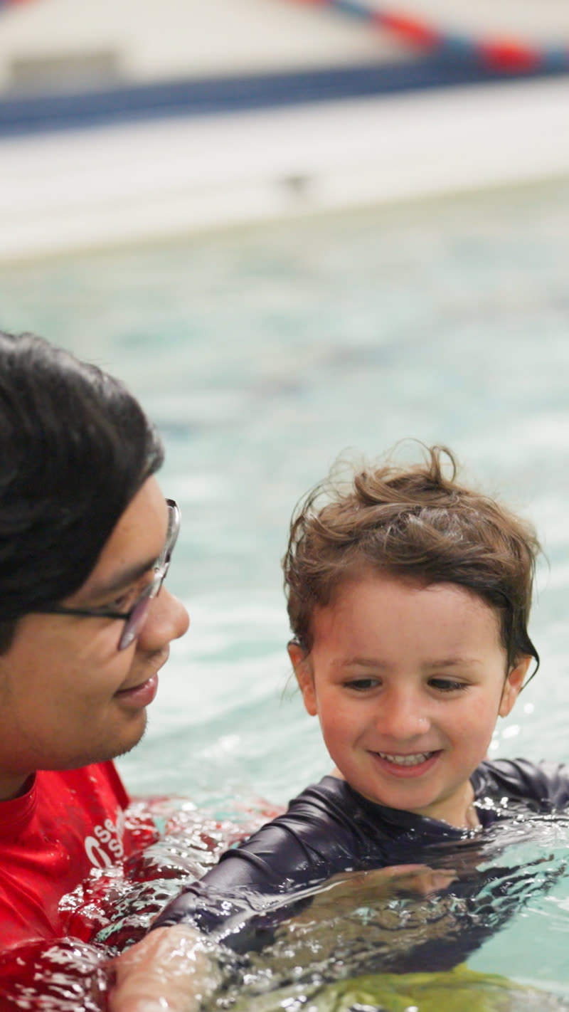 A swim teacher supports a smiling preschooler during a Seal Pups class.